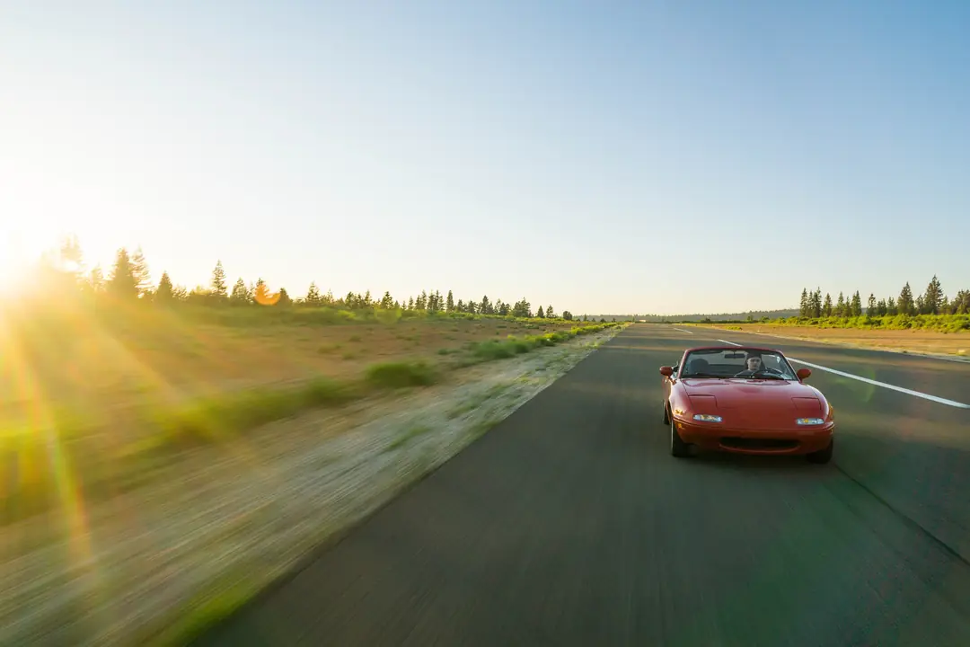 A red convertible driving down an open highway in bright late-day sun.